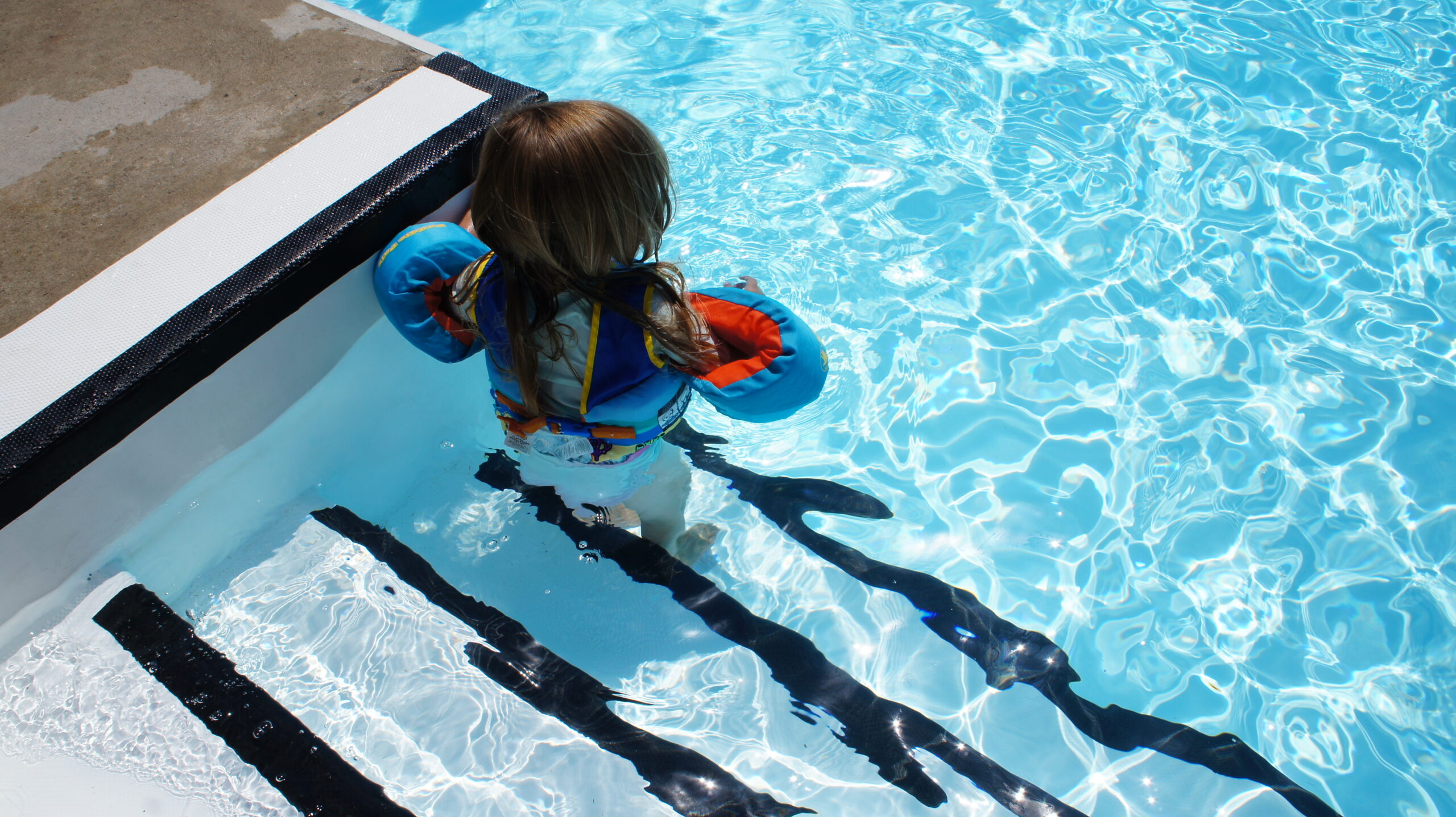 A little girl with life jacket standing on the anti-slip pool steps